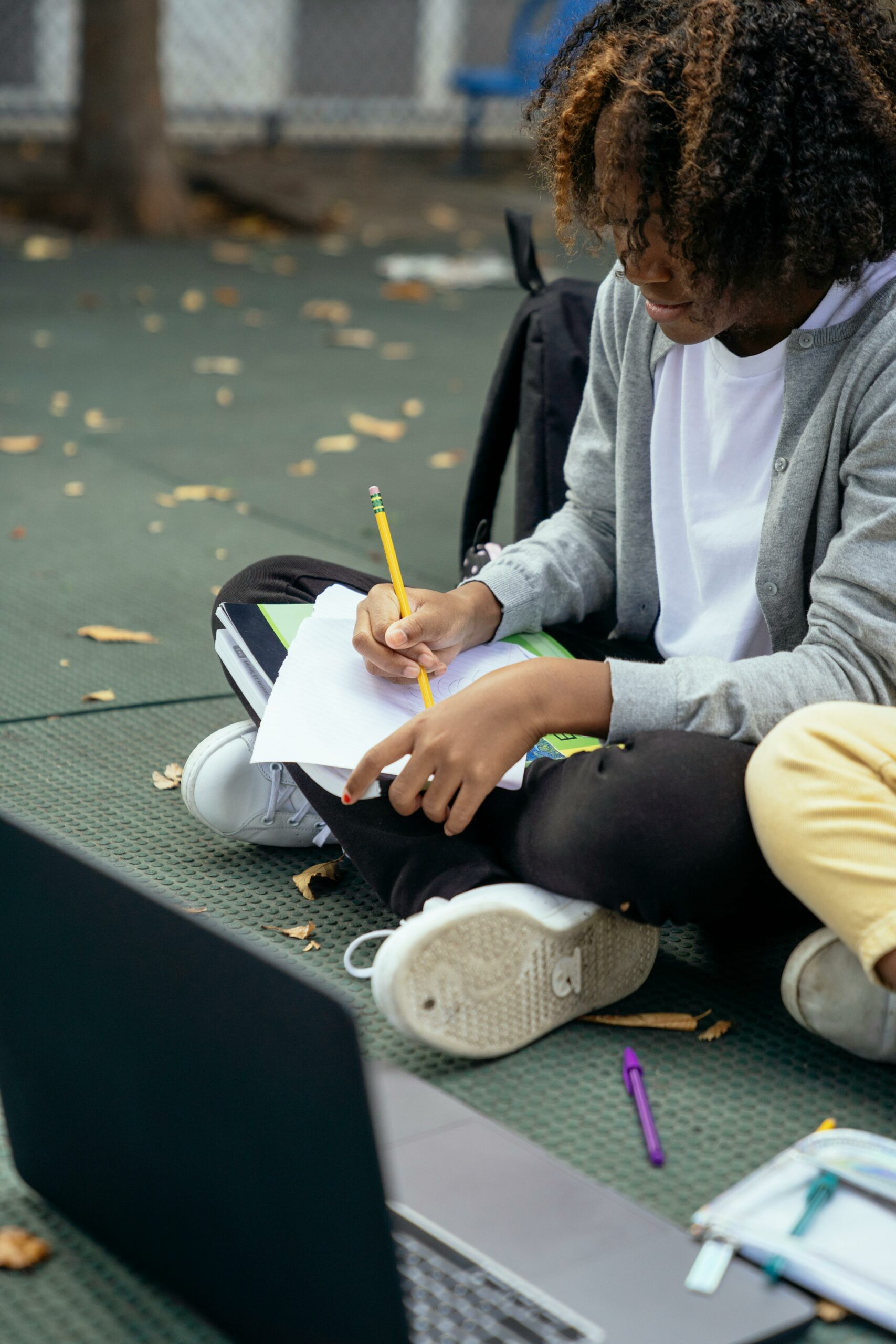 Young-black-teenage-student-working-in-the-school-playground-with-a school-laptop-beside-his-classmates
